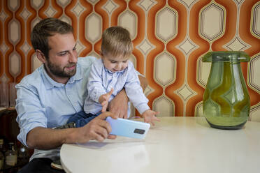 Vater macht Selfie mit dem Handy, während er seinen Sohn am Tisch trägt - DLTSF01728