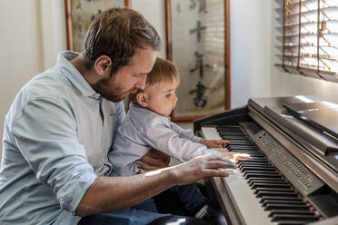 Vater gibt seinem Sohn Klavierunterricht, der zu Hause auf dem Schoß sitzt - DLTSF01732