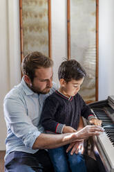 Father teaching piano to son sitting on lap at home - DLTSF01734