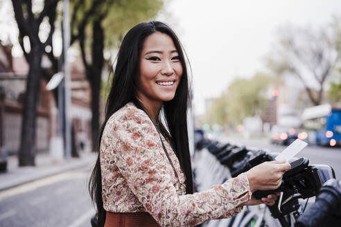 Lächelnde Frau, die über eine Karte in der Stadt ein Fahrrad mietet - EBBF03176