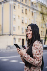 Smiling woman with smart phone in city - EBBF03217