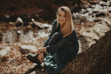 Beautiful woman sitting on retaining wall during autumn - GMLF01130