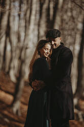 Boyfriend and girlfriend embracing in forest during sunny day - GMLF01135