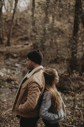 Couple with hands in pockets standing back to back in forest - GMLF01147