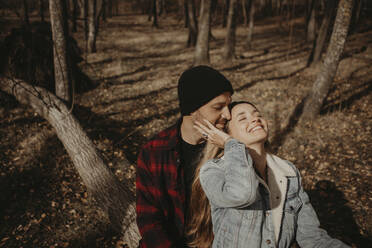 Couple sitting on tree in forest during sunny day - GMLF01148