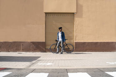 Lächelnder Mann mit Fahrrad, der wegschaut, während er an der Wand steht - AFVF08514