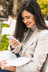 Smile female entrepreneur using smartphone in street while checking messages in email - ADSF22529