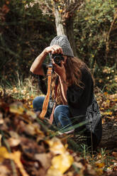 Mittlere erwachsene Frau beim Fotografieren mit Kamera im Wald im Herbst - MRRF01003