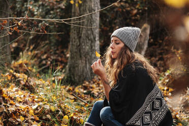 Beautiful woman with long hair blowing autumn leaf in forest during vacations - MRRF01004