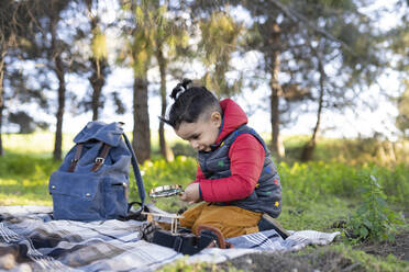 Neugieriger Junge, der auf einer Picknickdecke kniend ein Vergrößerungsglas durchsucht - JCCMF01807