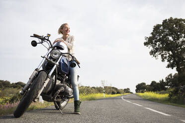 Lächelnde Motorradfahrerin, die auf dem Motorrad sitzend wegschaut - ABZF03520