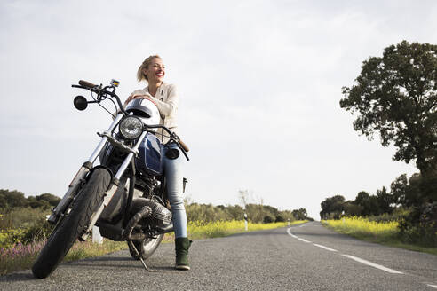 Smiling female biker looking away while sitting on motorcycle - ABZF03520