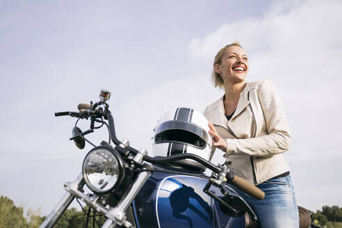 Happy female biker on motorcycle looking away - ABZF03521