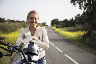Smiling female biker sitting with helmet on motorcycle - ABZF03522