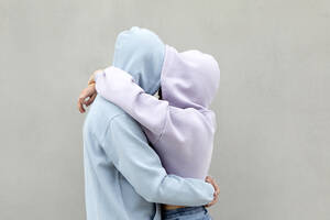 Couple in hooded shirt embracing each other by wall - PSTF00924