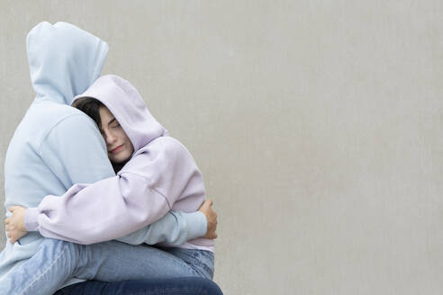 Girl embracing while sitting on boyfriend's lap by wall - PSTF00935