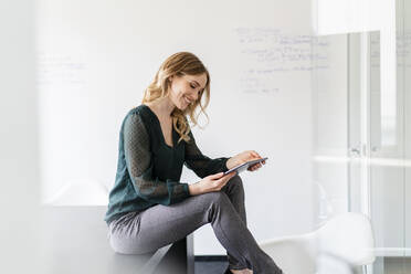 Contented businesswoman using digital tablet while sitting on conference table in office - DIGF15019