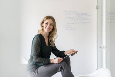 Happy female professional with digital tablet looking away while sitting in board room - DIGF15020