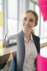 Lächelnde Unternehmerin mit Blick auf Haftnotizen im Büro - DIGF15024