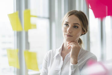 Female professional with hand on chin looking at adhesive note in office - DIGF15027