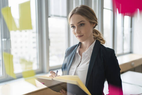 Weibliche Fachkraft plant Geschäftsstrategie beim Schreiben in Tagebuch im Büro - DIGF15029