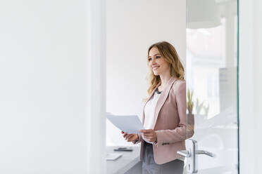 Female professional with document day dreaming while standing in office - DIGF15042