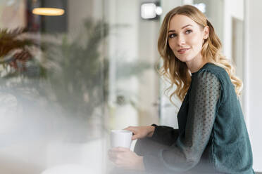 Weibliche Fachkraft, die Kaffee trinkt, während sie im Büro wegschaut - DIGF15072