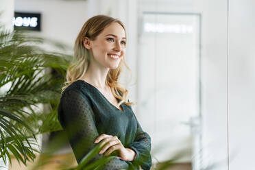 Smiling female entrepreneur with arms crossed looking away at office - DIGF15074