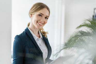 Schöne Unternehmerin lächelt, während sie ein digitales Tablet im Büro hält - DIGF15081