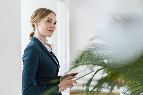 Contemplating female professional with digital tablet standing in office - DIGF15083