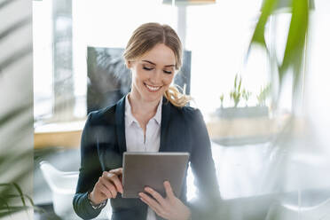 Zufriedene Geschäftsfrau bei der Arbeit am digitalen Tablet im Büro - DIGF15086