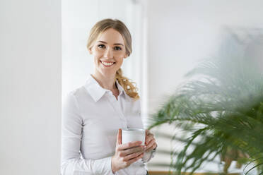 Smiling beautiful female professional holding coffee mug in office - DIGF15087