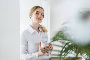 Businesswoman with eyes closed holding coffee mug in office - DIGF15090