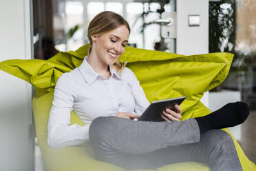 Female professional smiling while using digital tablet on bean bag in office - DIGF15092