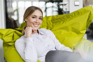 Contented businesswoman with hand on chin sitting on bean bag at office - DIGF15094