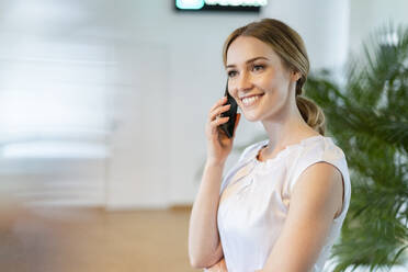 Lächelnde weibliche Fachkraft, die im Büro mit einem Mobiltelefon spricht - DIGF15099