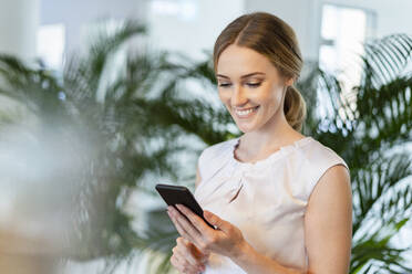 Happy businesswoman working on smart phone in office - DIGF15101