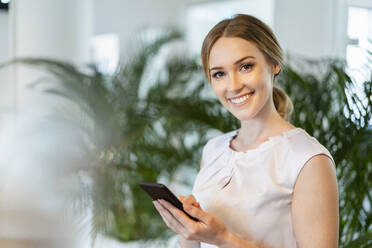 Lächelnde schöne Unternehmerin hält Smartphone im Büro - DIGF15102