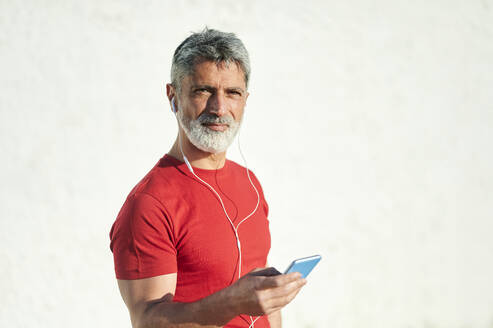 Hübscher Mann mit Smartphone an der Wand bei Sonnenschein - KIJF03696