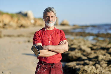Selbstbewusster Mann mit verschränkten Armen am Strand stehend an einem sonnigen Tag - KIJF03709
