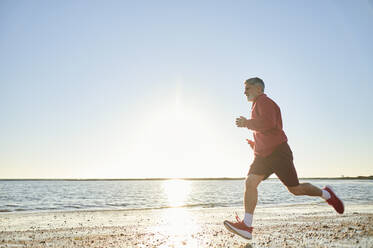 Männlicher Läufer, der bei Sonnenuntergang am Strand joggt - KIJF03722