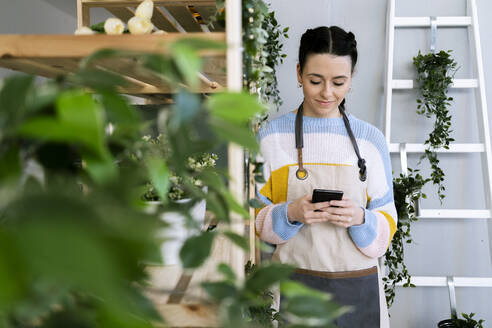 Frau benutzt Smartphone, während sie in der Nähe eines Regals in einer Werkstatt steht - GIOF12085