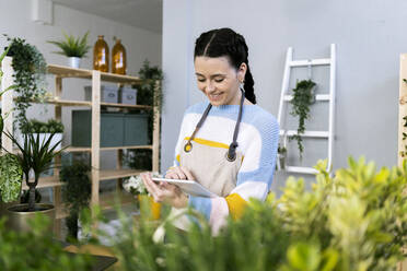 Lächelnde Gärtnerin mit digitalem Tablet in der Werkstatt - GIOF12089