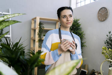 Nachdenkliche Frau mit Tasse in der Hand in einer Werkstatt stehend - GIOF12094