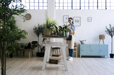 Female gardener standing by wall while working in workshop - GIOF12095