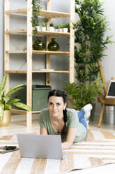Young woman with laptop lying on floor at home - GIOF12115