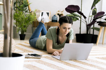 Beautiful woman using laptop while lying on carpet at home - GIOF12116