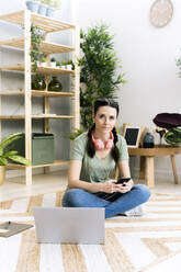 Frau mit Smartphone sitzt zu Hause am Laptop - GIOF12119
