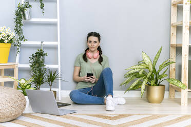 Junge Frau inmitten von Pflanzen an der Hauswand sitzend - GIOF12122