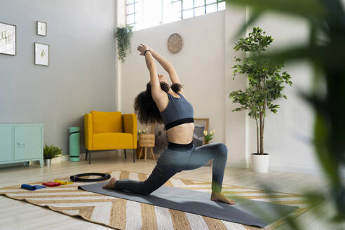 Woman practicing sun salutation on exercise mat in living room - GIOF12146